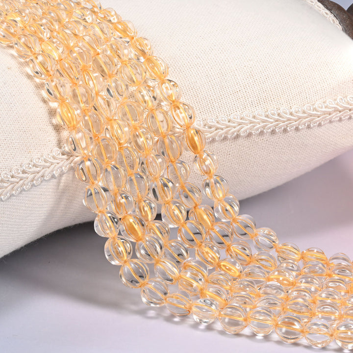 Clear gold pumpkin glass beads, 8mm fluted melon rounds, several strands draped over a white cushion.