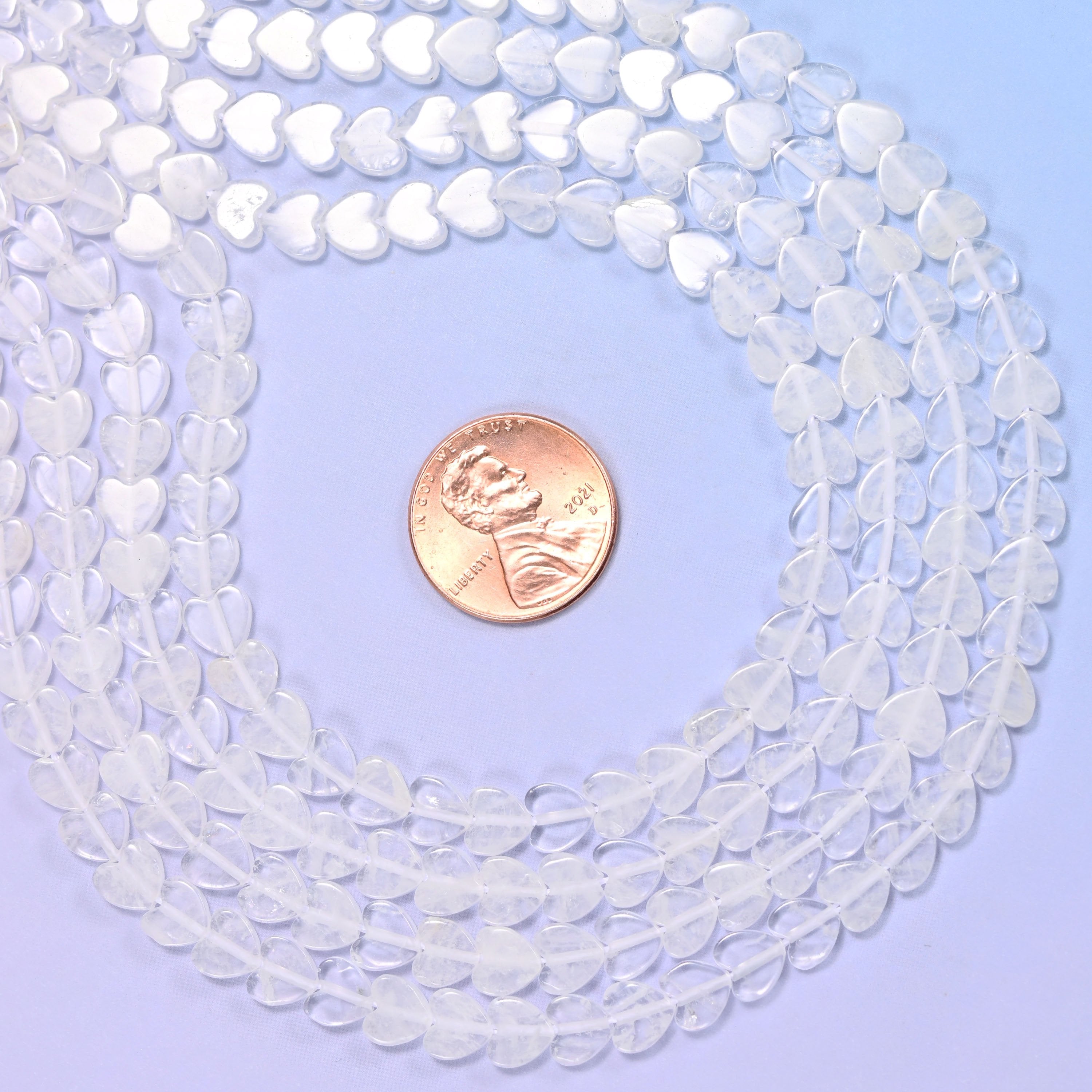 Tiny flat hearts in colourless quartz, mostly frosted-looking ice white with a few beads clear enough to see straight through, polished smooth on both faces.