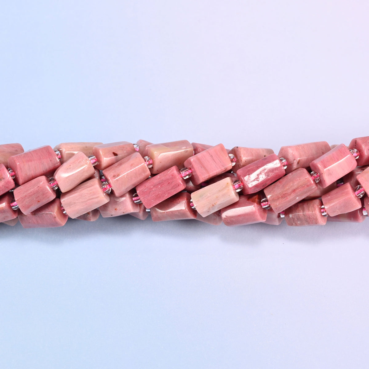 Close-up of Pink Rhodonite faceted tube beads showing the flat cut planes, polished surface and pink glass seed bead spacers