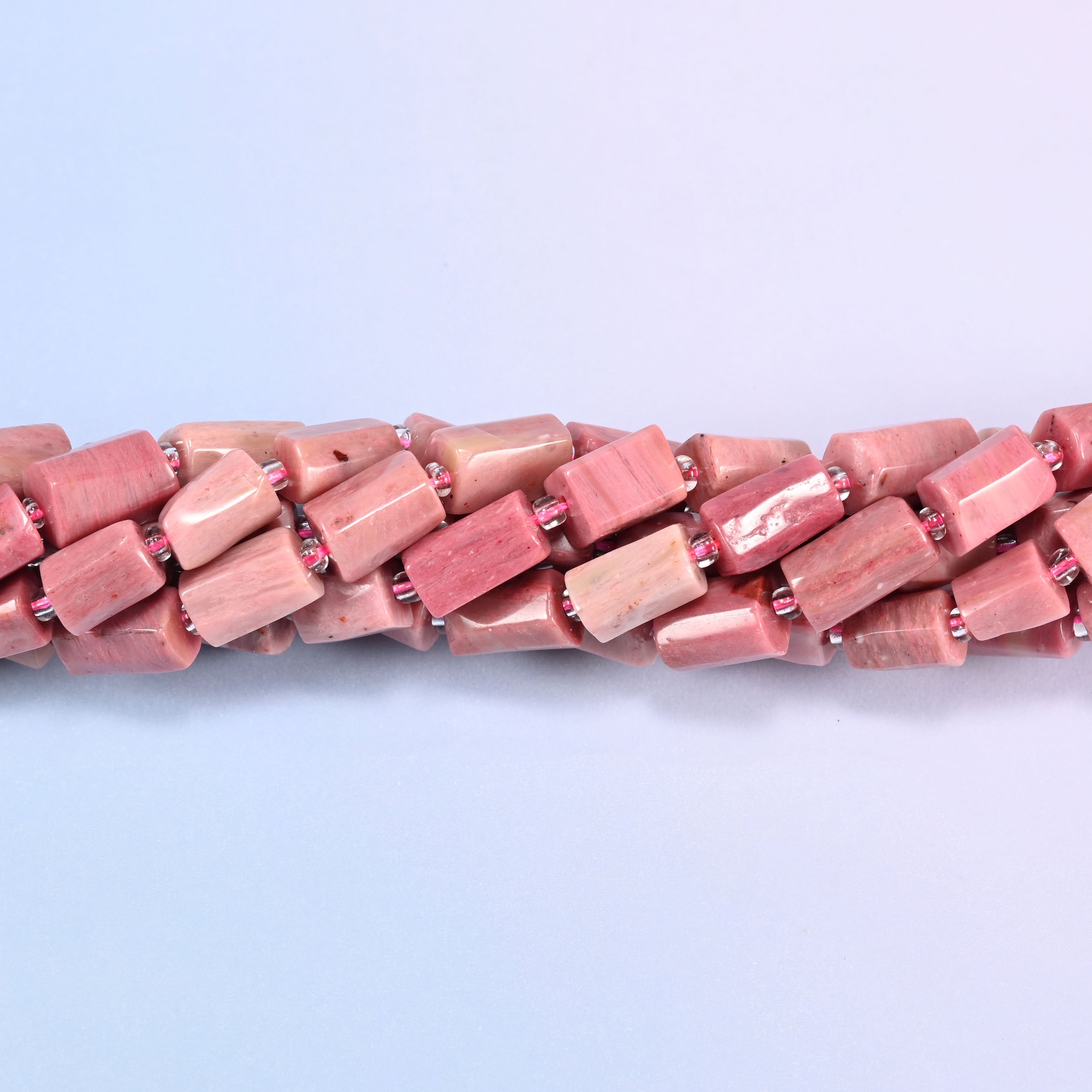 Close-up of Pink Rhodonite faceted tube beads showing the flat cut planes, polished surface and pink glass seed bead spacers
