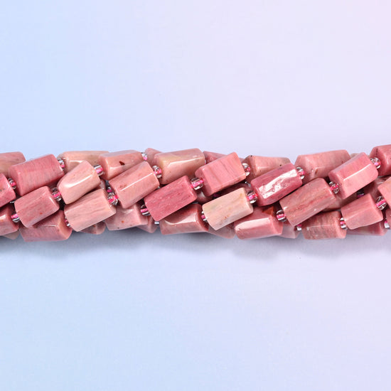 Close-up of Pink Rhodonite faceted tube beads showing the flat cut planes, polished surface and pink glass seed bead spacers