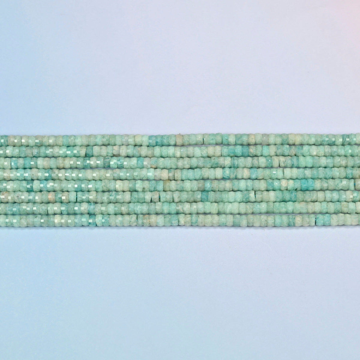 Several strands of green amazonite faceted heishi disc beads laid in straight rows