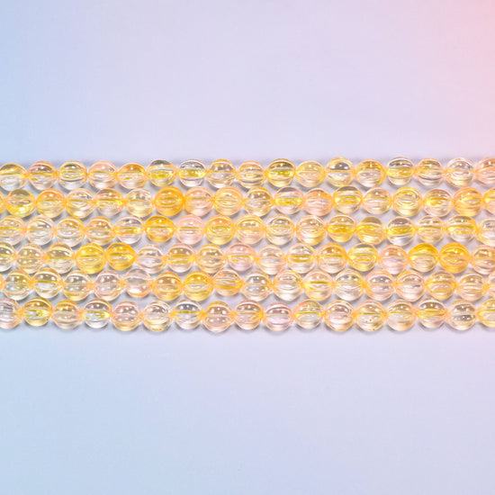 Close-up of 8mm yellow clear pumpkin glass beads in four horizontal rows, showing the carved melon ribs.