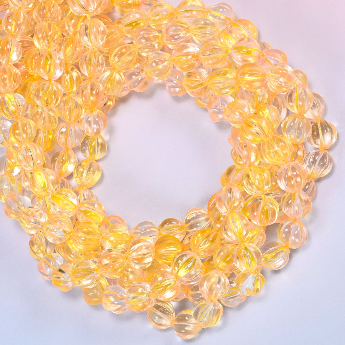 Yellow clear pumpkin glass beads coiled with the open center to one side, showing the fluted grooves end on.
