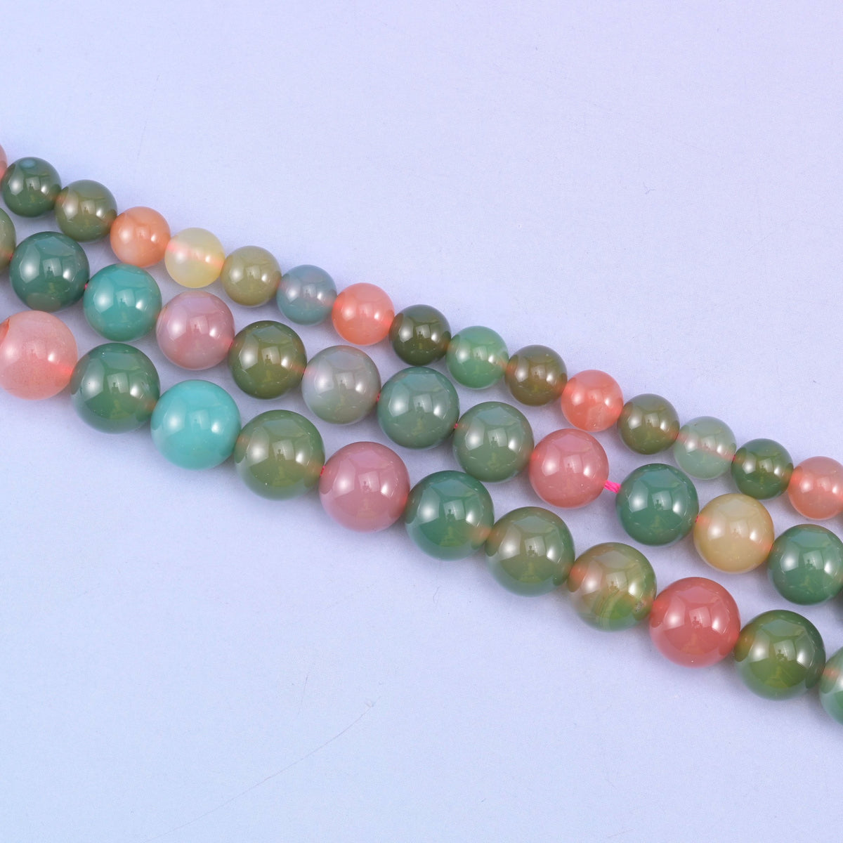 Green Yanyuan Agate smooth round beads, strands laid in diagonal rows on a lilac background, lightly translucent with a glossy polish