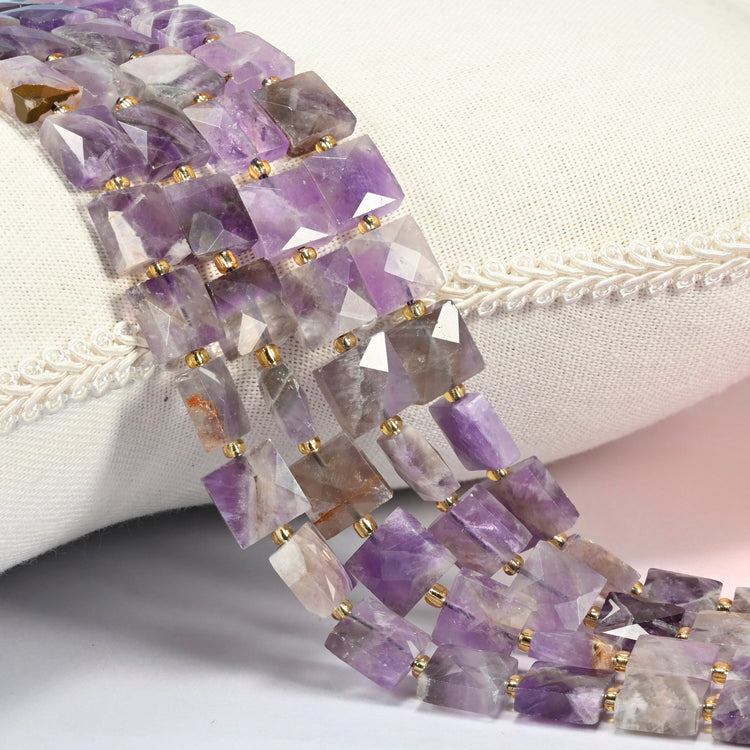 Natural amethyst faceted flat square beads 10x10mm with small gold seed bead spacers, several strands draped over a white cushion