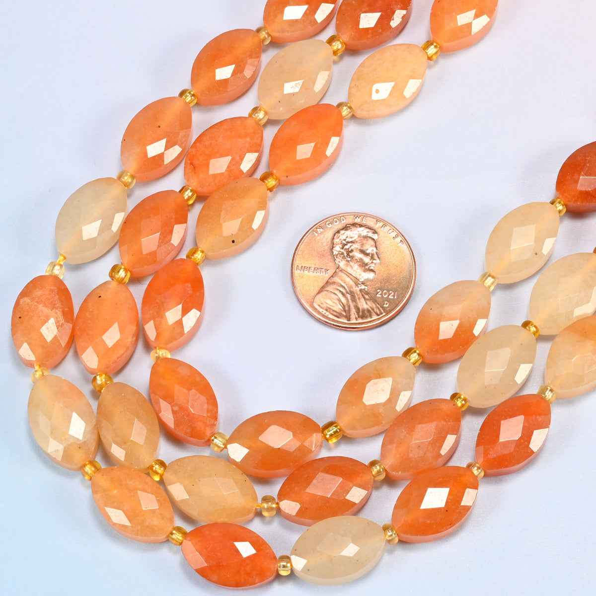 Close view of red aventurine faceted flat oval strands curving beside a US penny for scale