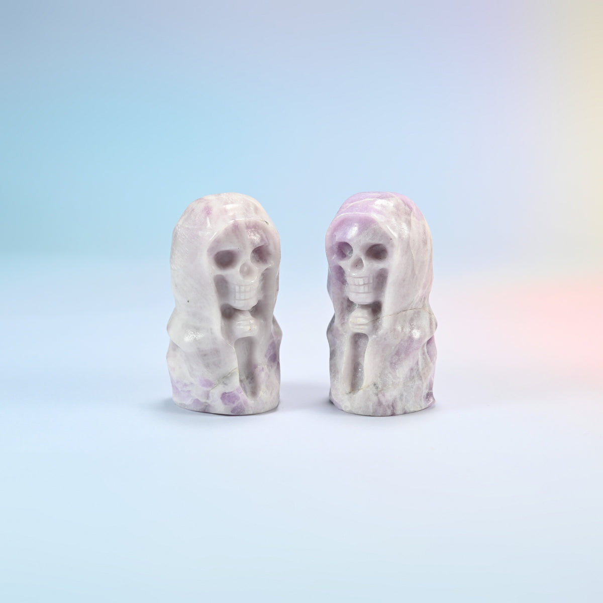 Two natural lepidolite hooded skull carvings, white with lilac and purple spots