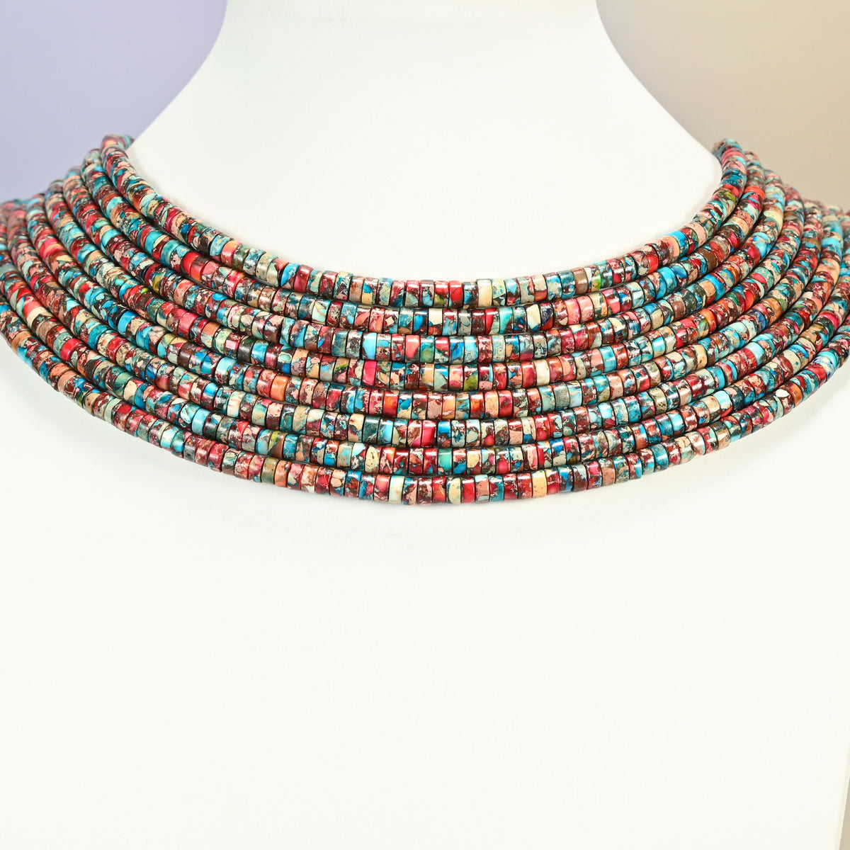 Dyed red blue sea sediment jasper heishi disc strands arranged as a layered collar on a white display bust