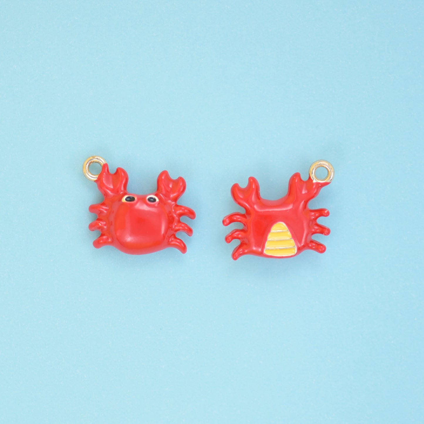 Enamel crab charms in bright red with black eyes and an 18K gold plated ring, shown front and back with the yellow striped underside