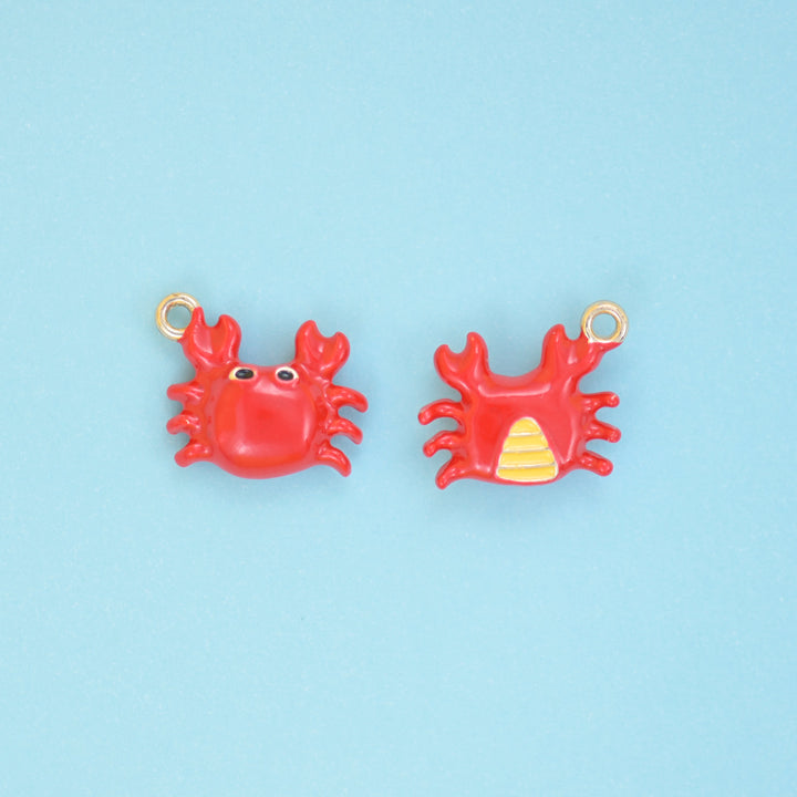 Enamel crab charms in bright red with black eyes and an 18K gold plated ring, shown front and back with the yellow striped underside