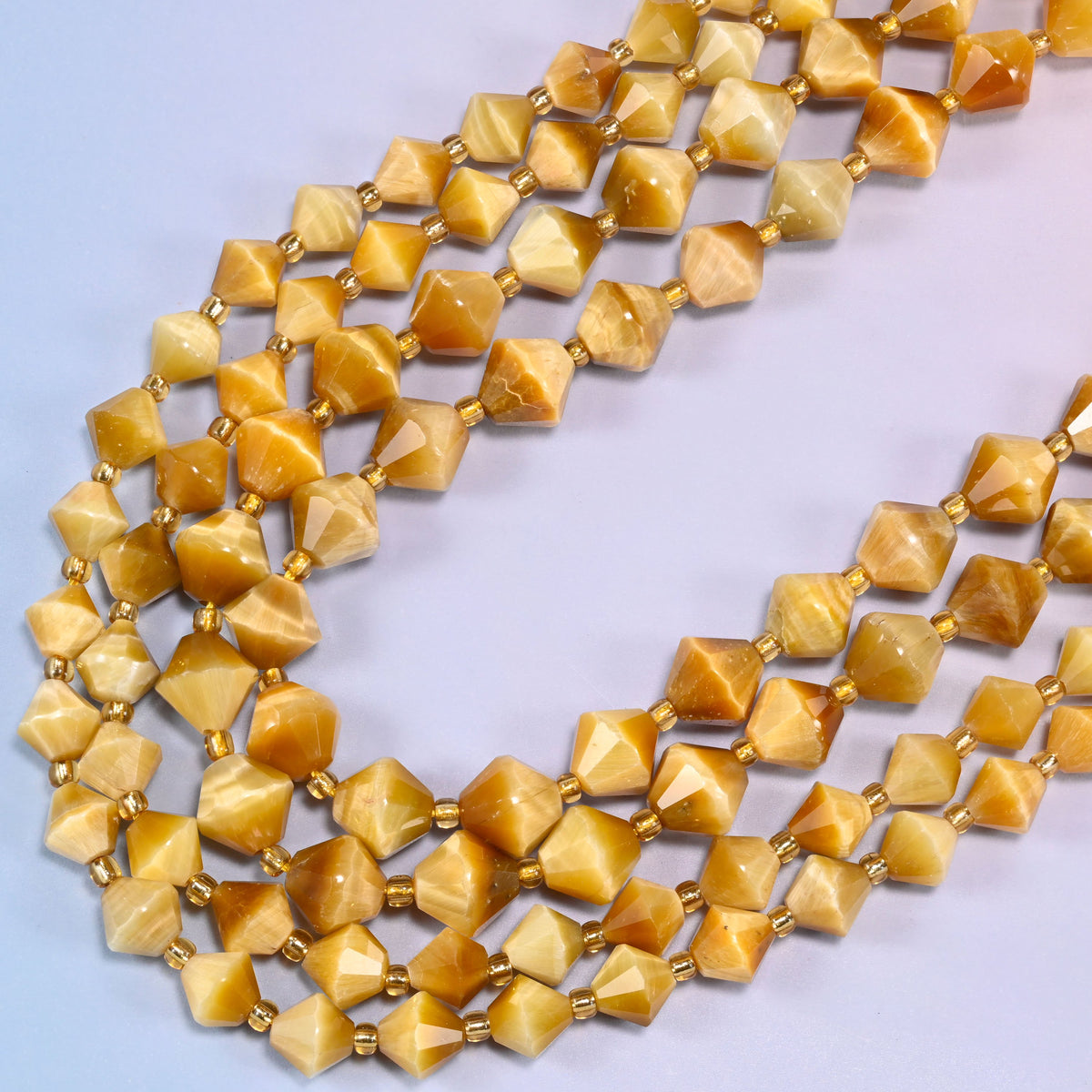 Gold tiger eye bicone beads in a wide loop curving down and back, pale butterscotch beads next to deeper amber ones.