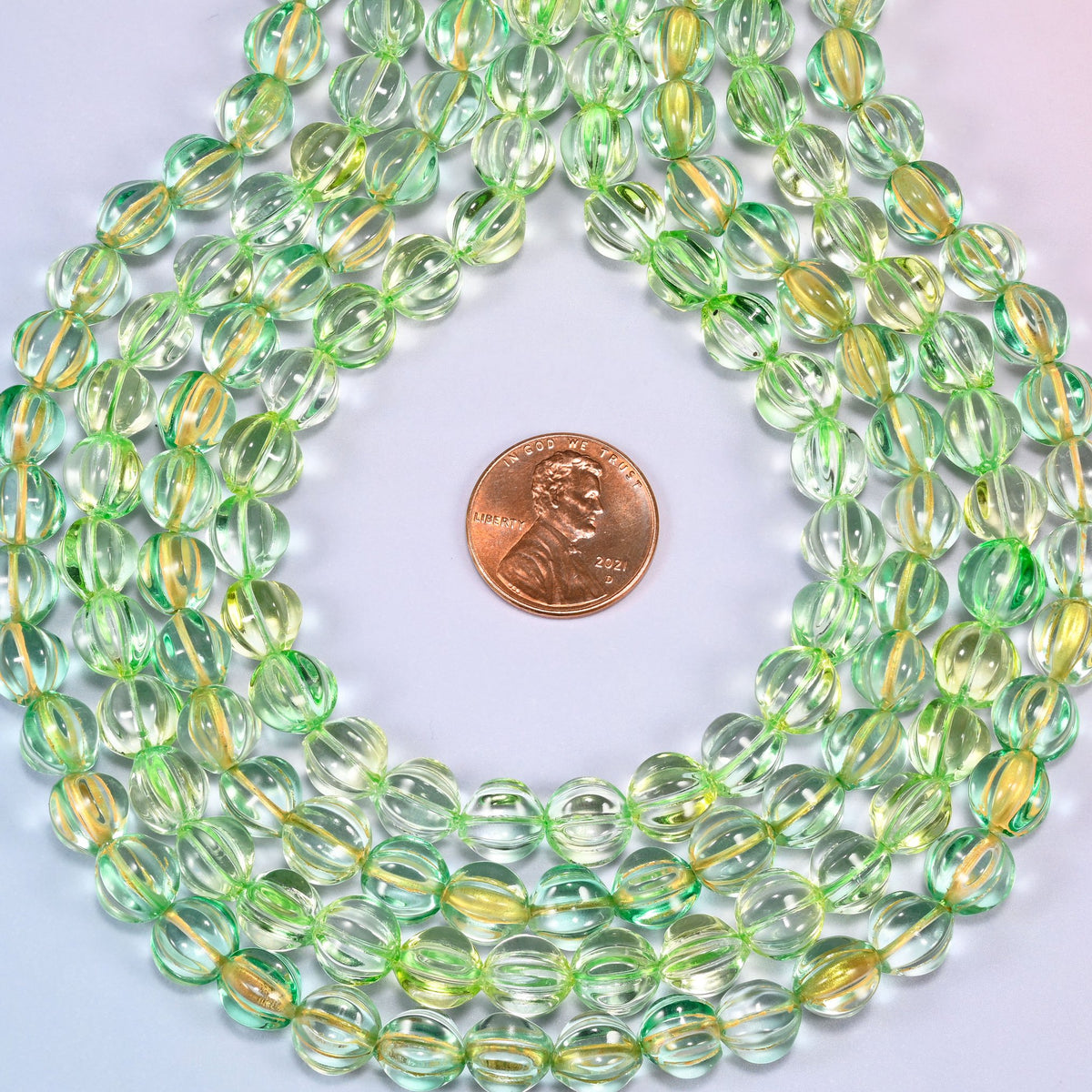 Green gold pumpkin glass beads, 8mm melon rounds, strands laid in a gentle wave straight across the frame.
