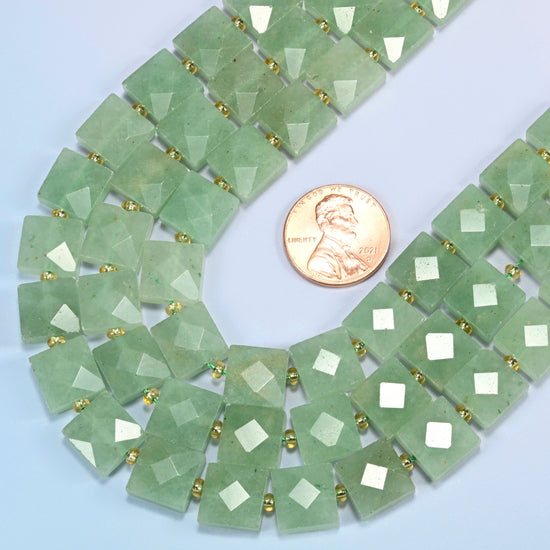 Close view of natural green aventurine faceted flat square strands curving beside a US penny for scale
