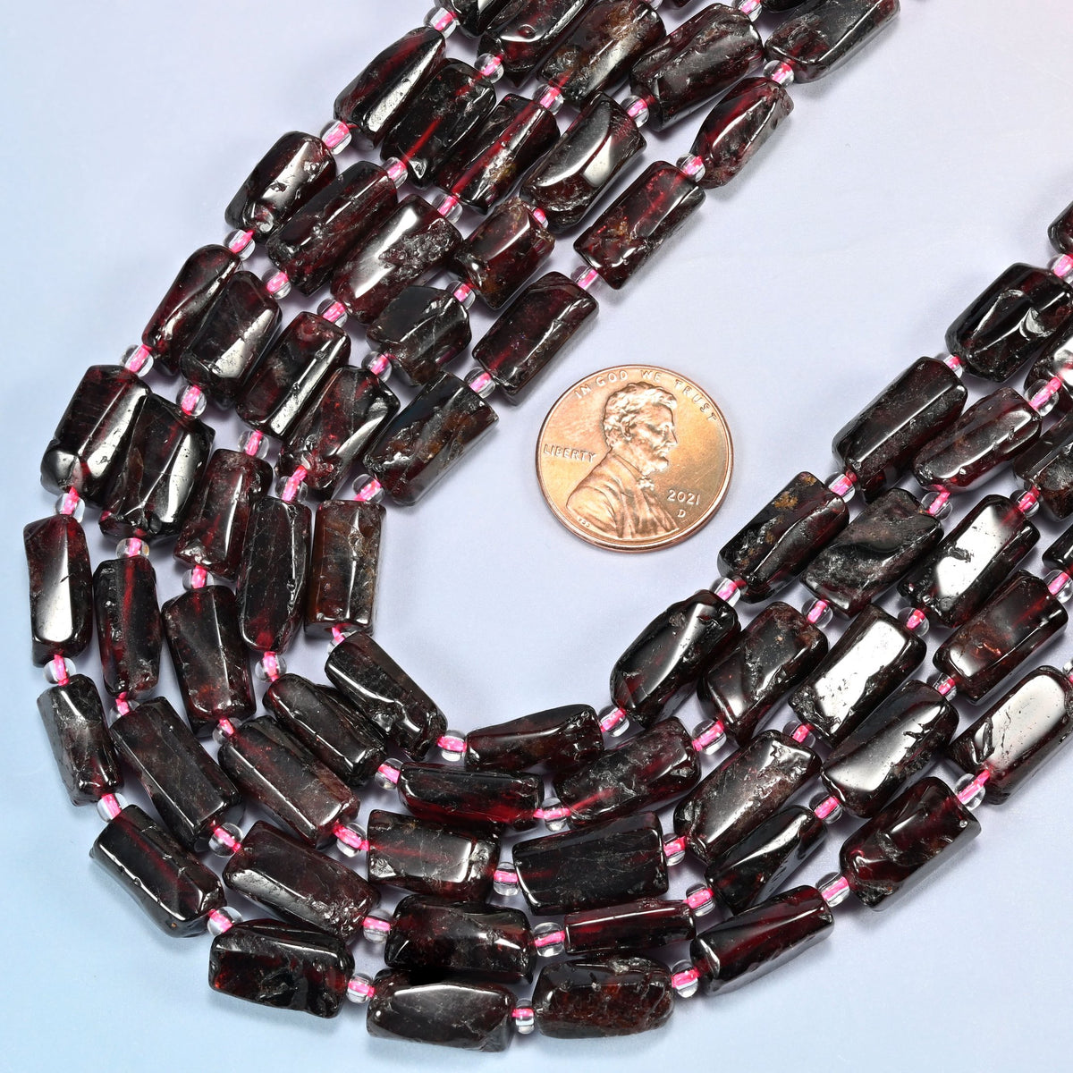 Close view of red garnet tube strands curving beside a US penny for scale