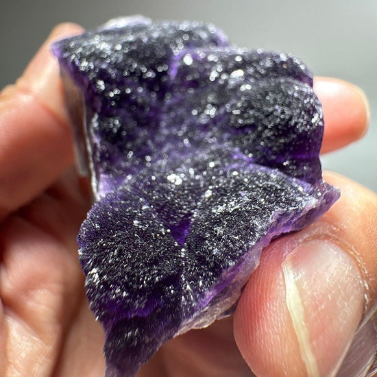 Dark purple fluorite mineral specimen with frosted quartz crust across the upper face.