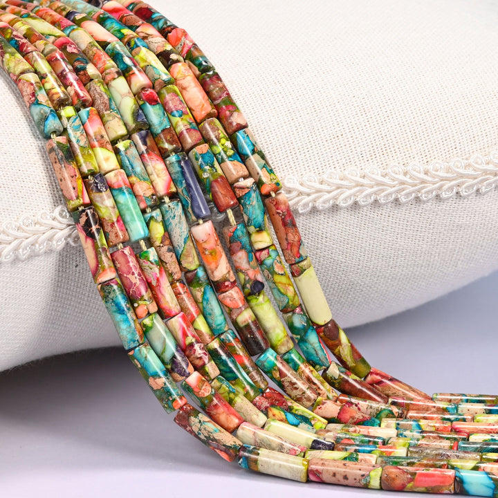 Close-up of multiple strands of multicolor dyed Sea Sediment Jasper tube beads draped over a cream fabric jewelry display bust, showing turquoise, coral, olive, and cream patterned beads.
