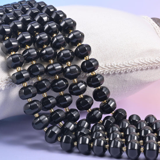Black obsidian pumpkin rondelle strands on a cream cushion, glossy ribbed beads with gold spacers