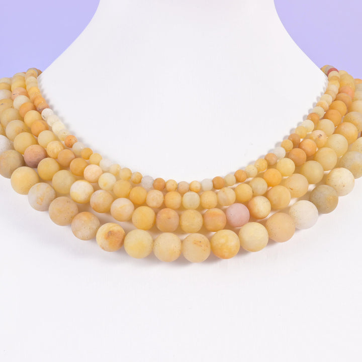 Yellow Jade matte round beads laid across a white necklace display, offered in 4mm, 6mm, 8mm and 10mm