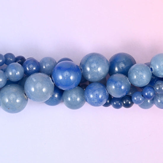 Denim blue rounds that run from pale powder to deep ink across a single strand, some beads flecked with darker navy, all polished smooth and evenly glossy. Straightforward