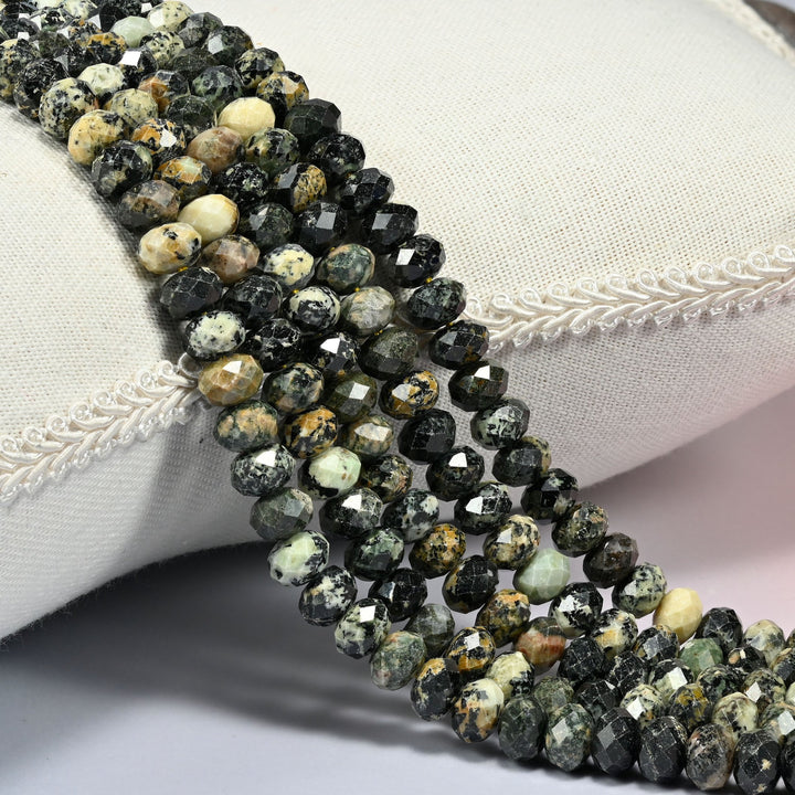 Old African howlite faceted rondelle beads 5x8mm in near-black speckled with cream and tan, several strands draped over a white cushion