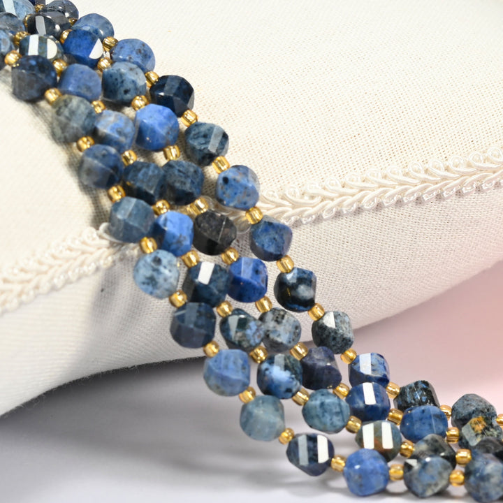 Blue dumortierite faceted spiral twist beads 8mm with small gold spacer beads, several strands draped over a white cushion