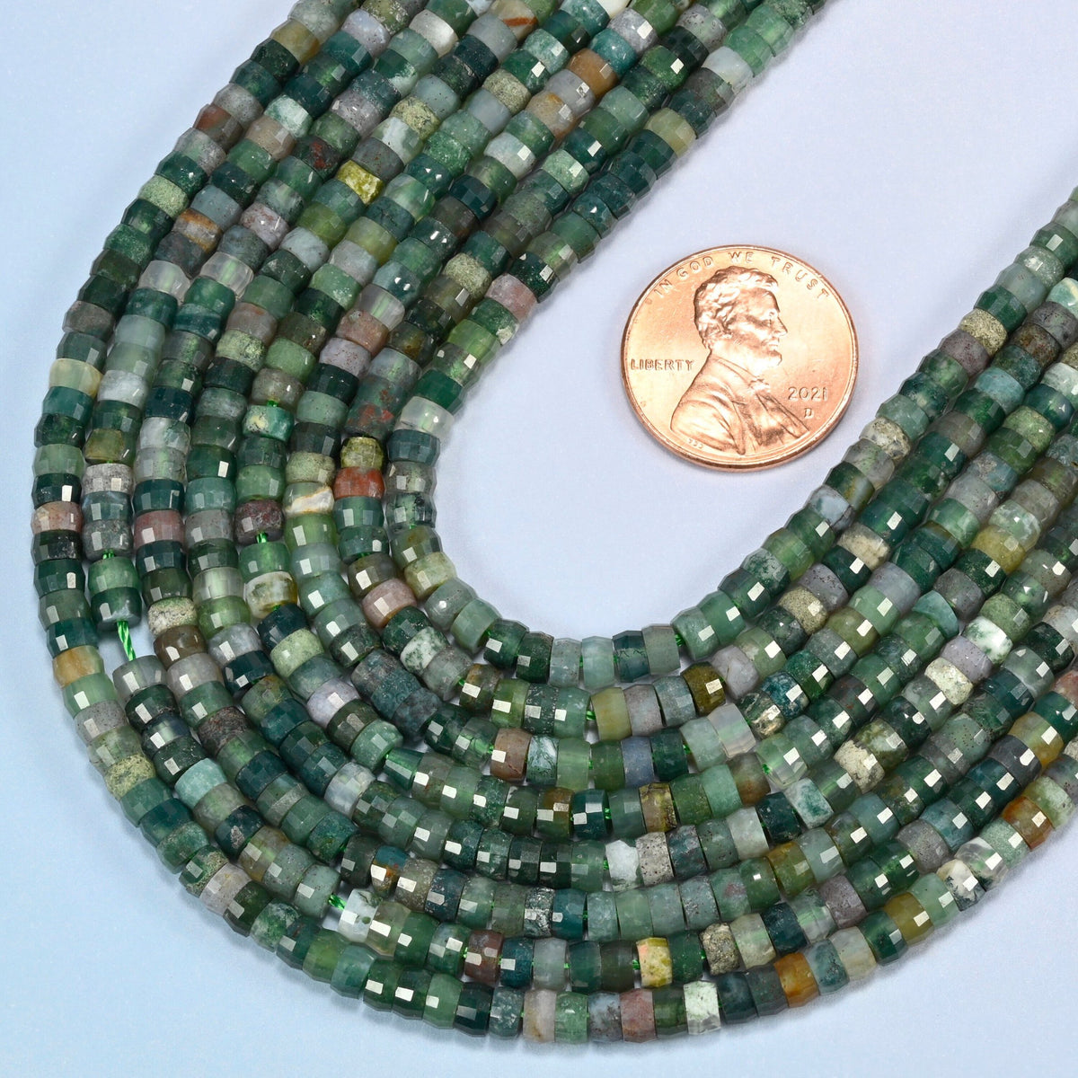 Close view of Indian agate faceted heishi disc strands curving beside a US penny for scale