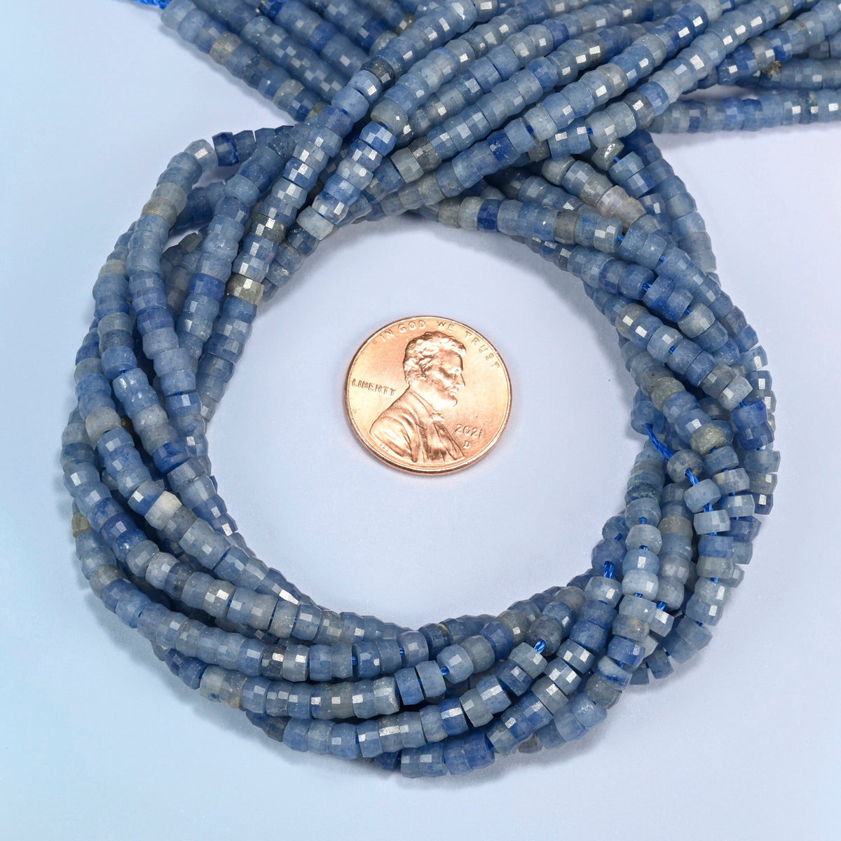 Blue aventurine faceted heishi disc beads 2x4mm coiled in a loop around a US penny for scale, close-up of the faceted disc shape