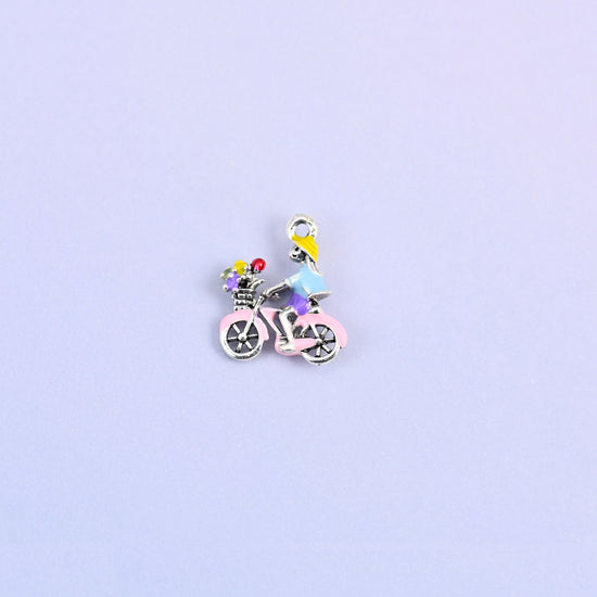 Bicycle charm with a yellow haired rider in a light blue top and a green flower basket on the front.