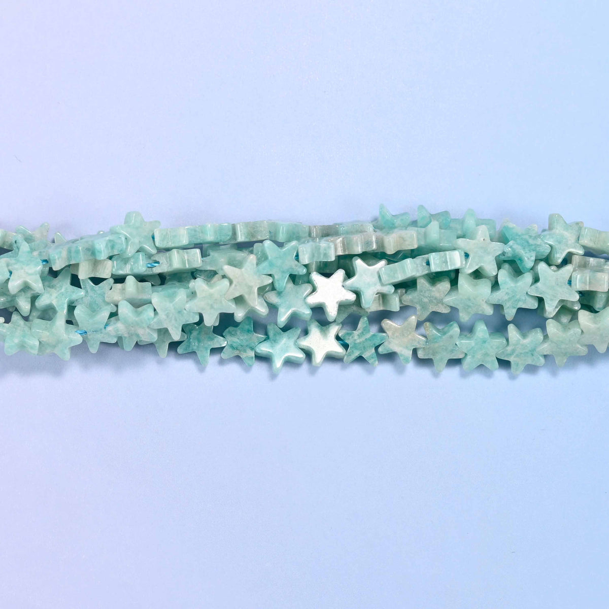 A chalky seafoam blue-green lightly mottled with white and the odd tan fleck, cut into small flat five-pointed stars whose matte-satin surface keeps the color soft rather than glassy.