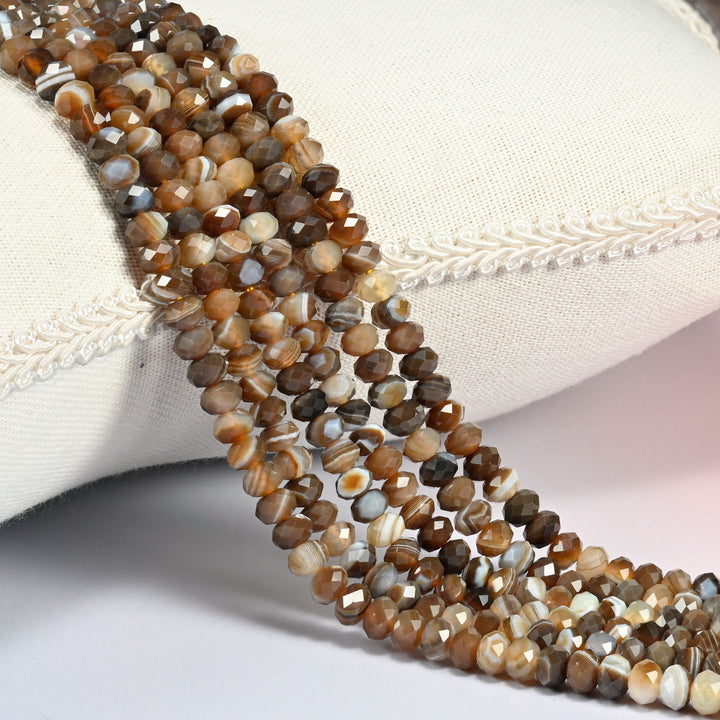 Dyed Brown Strip Agate gemstone rondelle beads 4x6mm faceted, strand draped over a cream fabric cushion