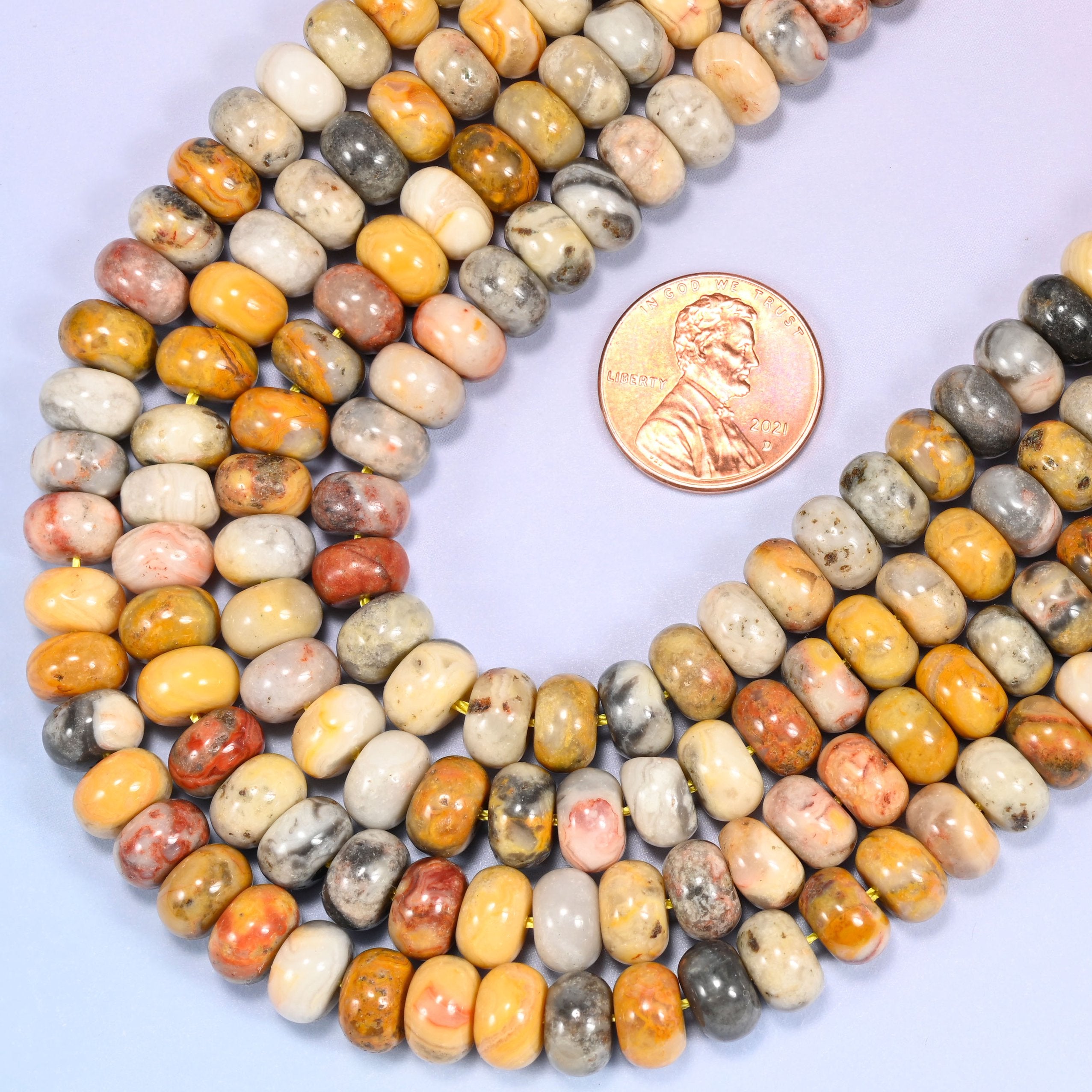 Circular coil of Crazy Agate bead strands on a lavender background with a penny in the center for size comparison.