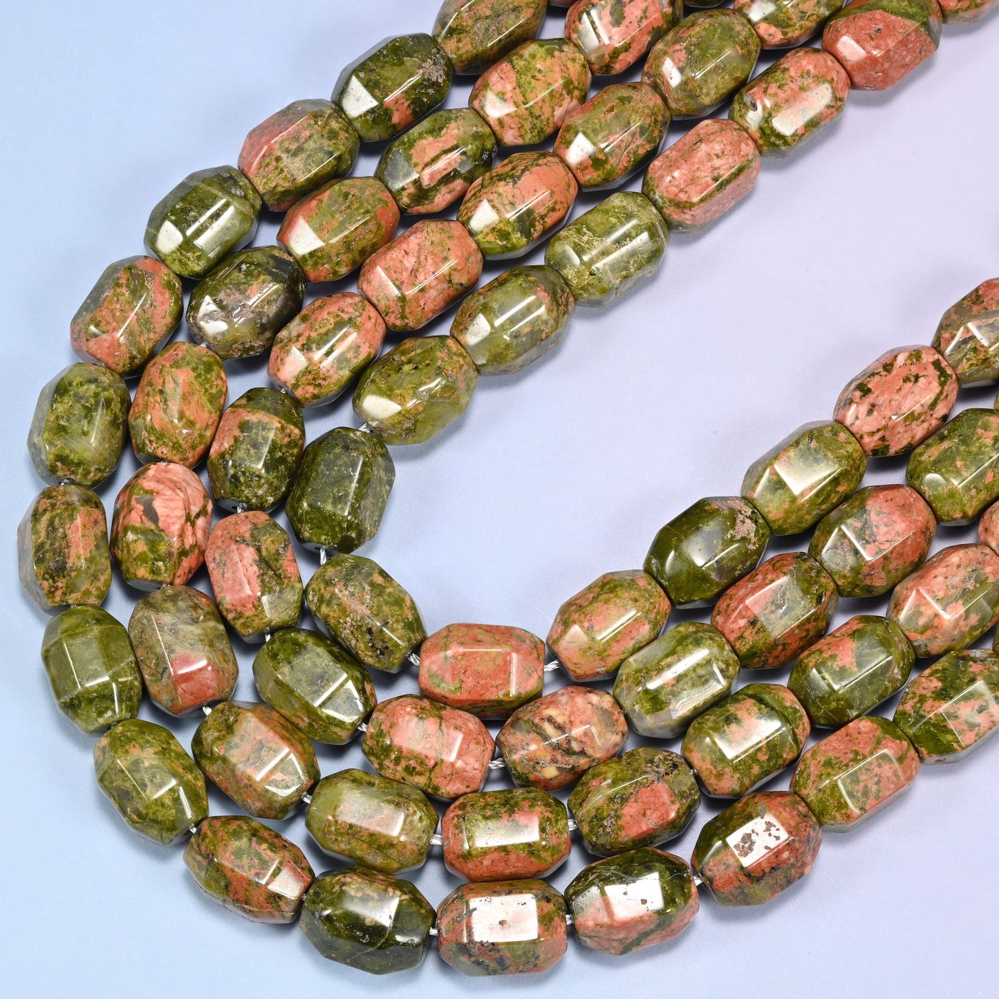 Wider rows of faceted Unakite barrel beads on a light blue background, showing size and color variation.