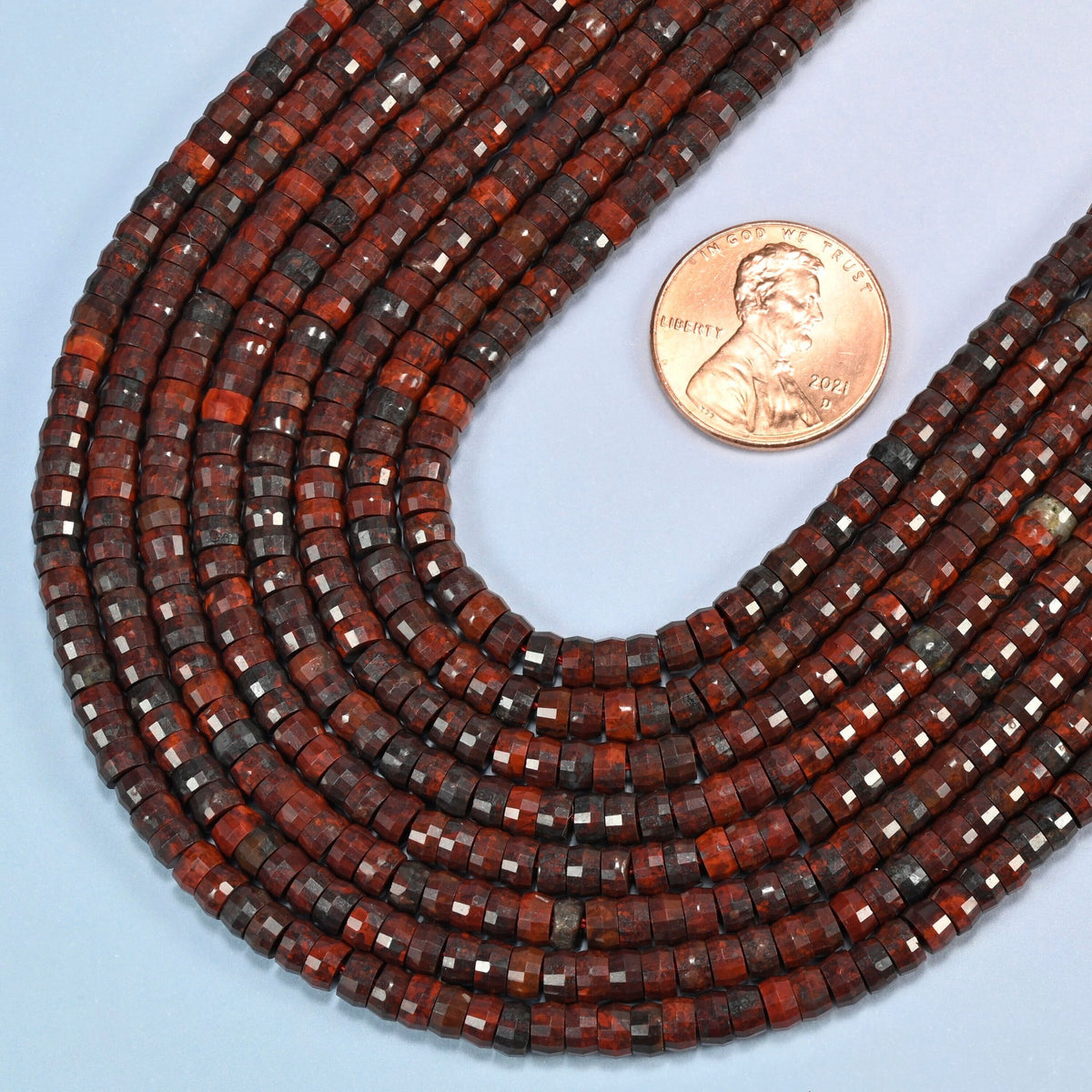 Close view of Zhanguo red agate faceted heishi disc strands curving beside a US penny for scale