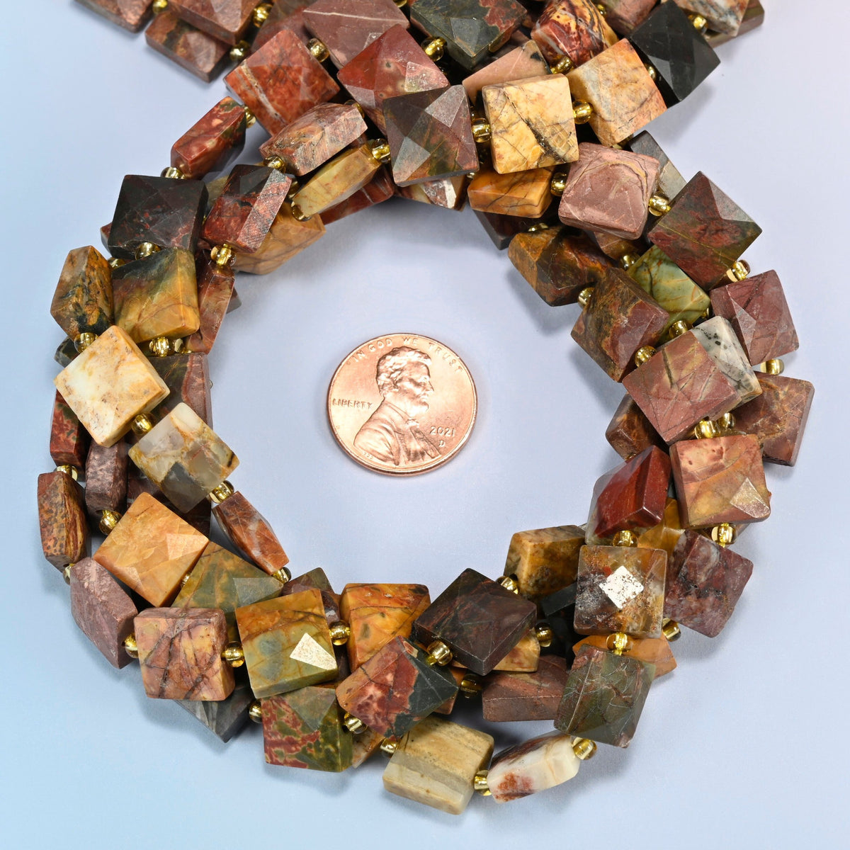 Natural red howlite faceted flat square beads 10x10mm coiled in a loop around a US penny for scale, close-up of the faceted flat square shape