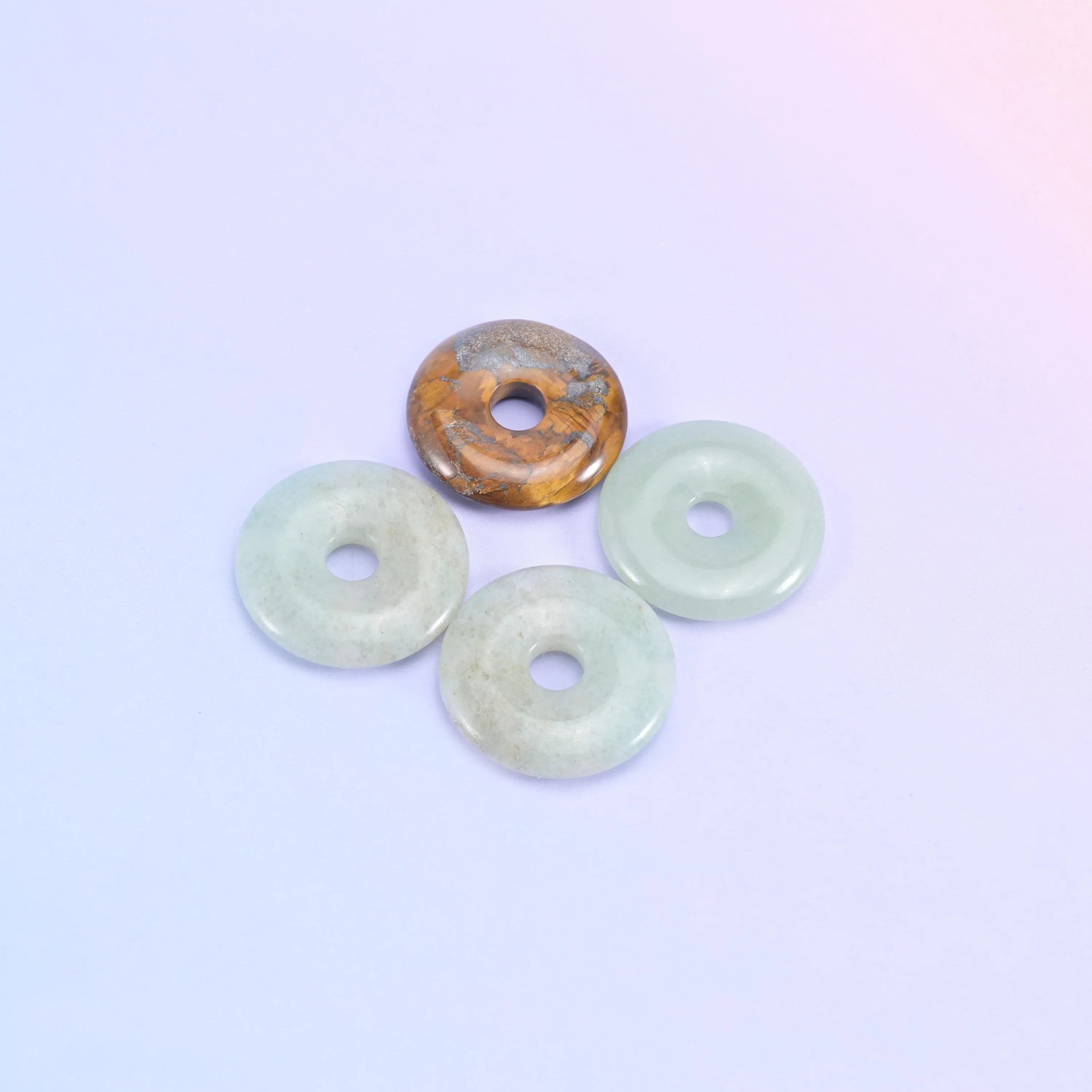 Three pale green donuts with one banded tiger eye donut resting on top