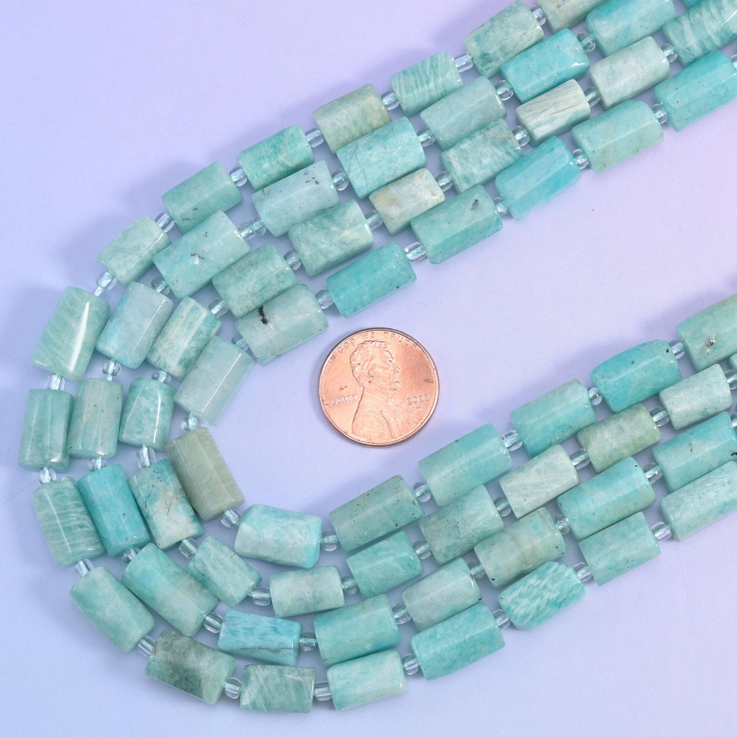 Amazonite faceted tube strands looped beside a US penny, giving a clear sense of the 12x8mm bead size