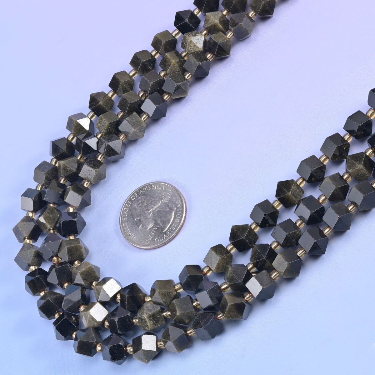 Faceted 8 sides diamond rhombus beads in gold obsidian beside a US quarter laid flat for scale.