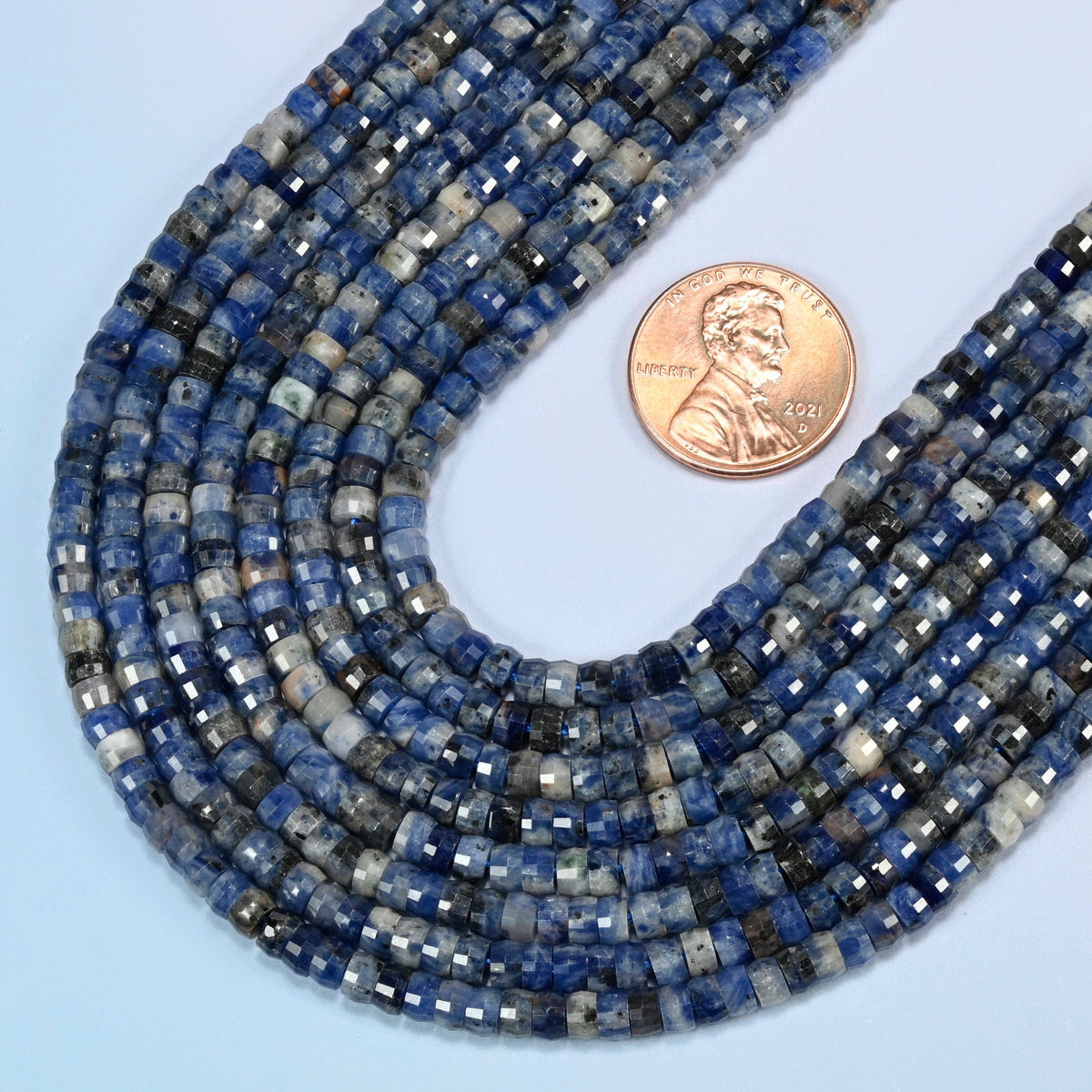 Close view of sodalite faceted heishi disc strands curving beside a US penny for scale
