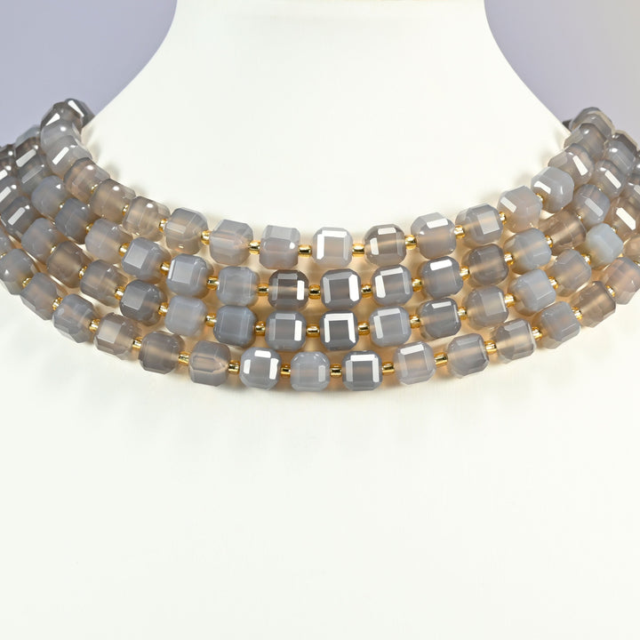 Gray agate faceted cube strands arranged as a layered collar on a white display bust, soft translucent gray beads across the neck