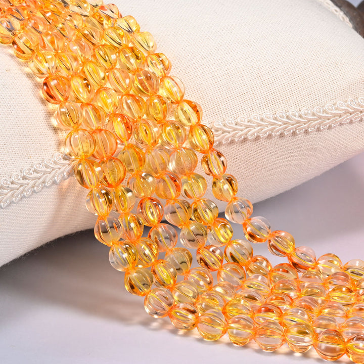 Yellow gold pumpkin glass beads, 8mm fluted melon rounds, several strands draped over a white cushion.
