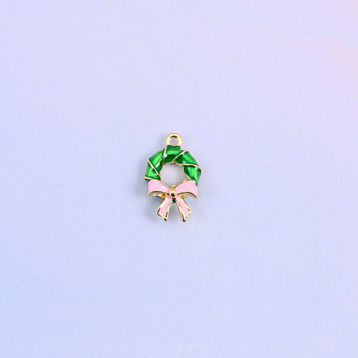 Green enamel wreath charm with a light pink bow, the ring twisted like a wound garland with gold banding between the turns.
