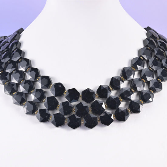 Faceted obsidian hexagons layered on a display bust, forming a dark geometric collar