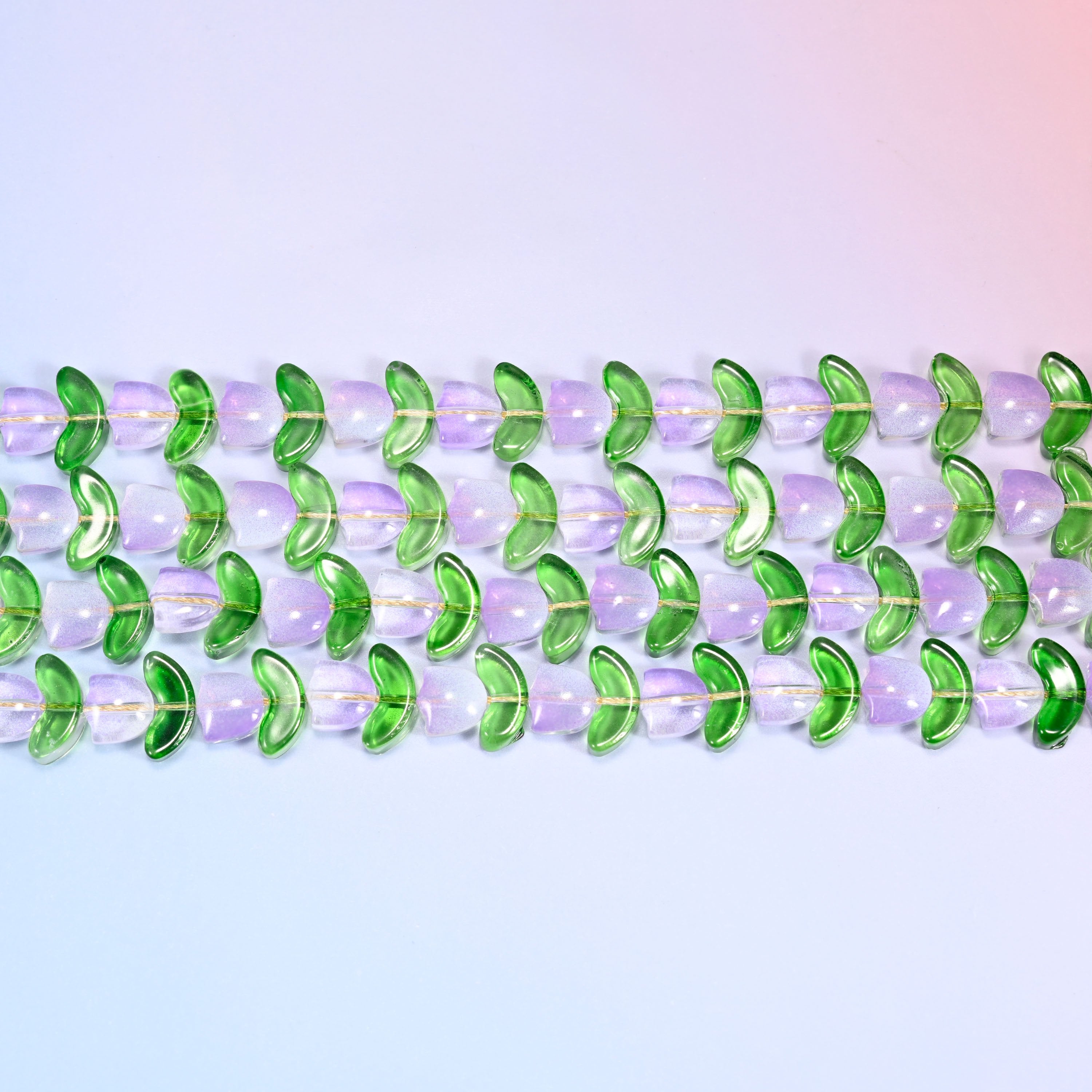 Close-up macro view of lavender tulip and green leaf glass beads in a dense repeating row pattern on a lavender and pink gradient background.
