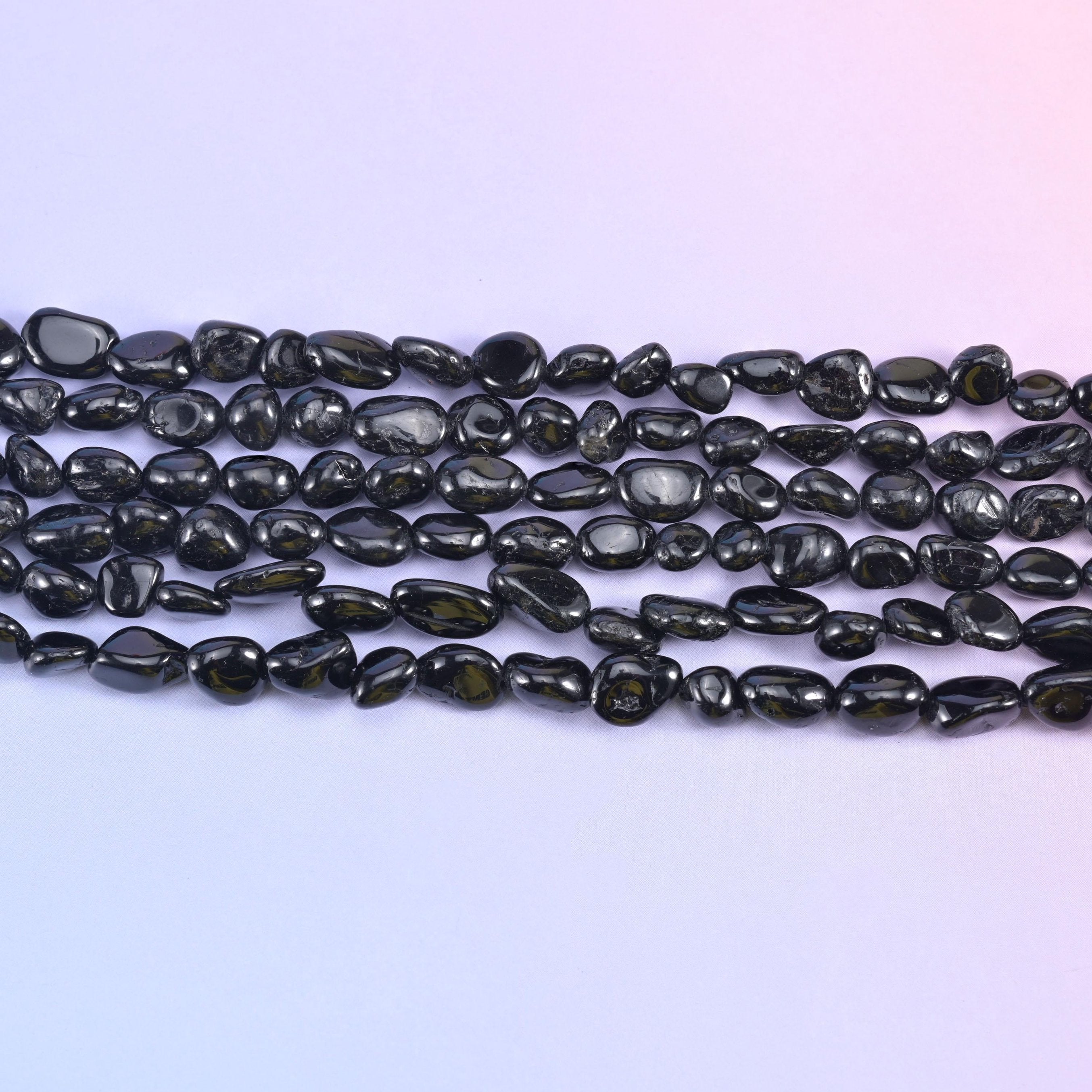 Rows of glossy black tourmaline nuggets on a pale lavender background