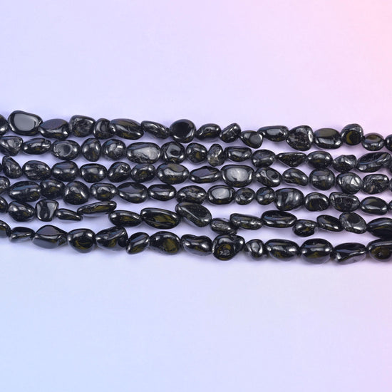 Rows of glossy black tourmaline nuggets on a pale lavender background