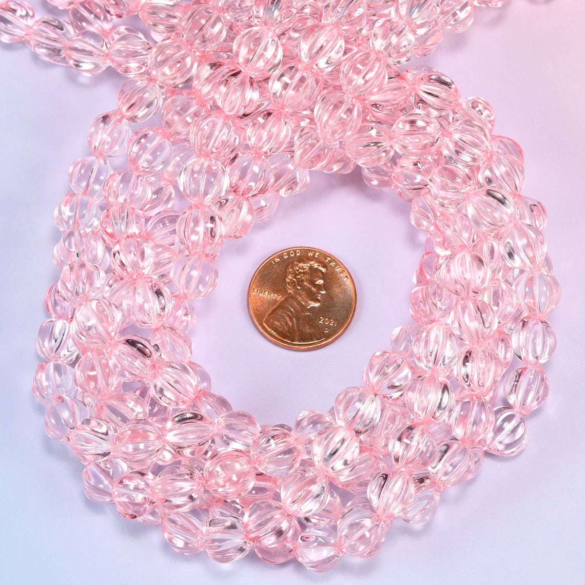 Clear pink pumpkin glass beads coiled tightly, shown with a US penny in the open center for scale.