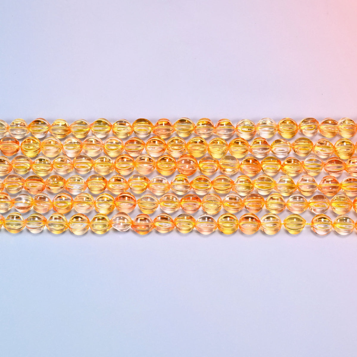 Close-up of 8mm yellow gold pumpkin glass beads in four horizontal rows, showing the carved melon ribs.