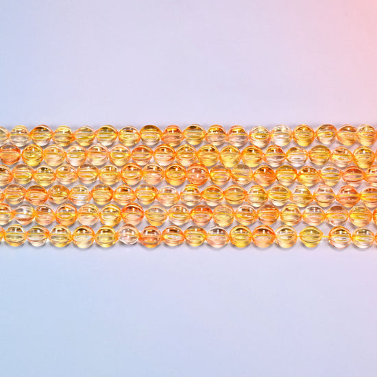 Close-up of 8mm yellow gold pumpkin glass beads in four horizontal rows, showing the carved melon ribs.