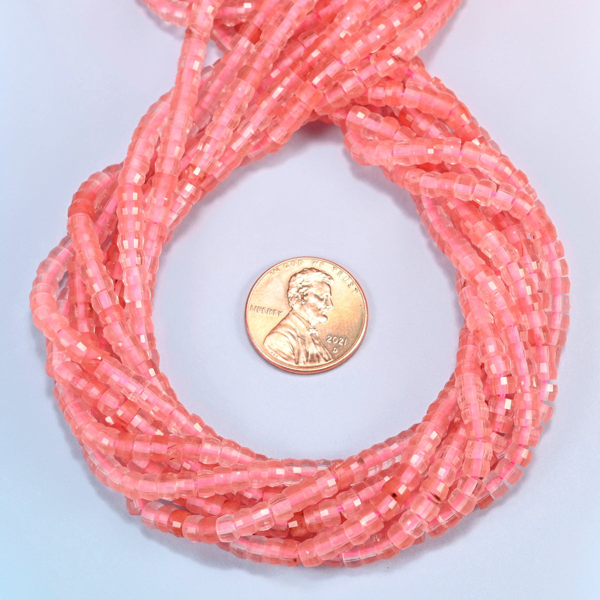Melon quartz faceted heishi disc beads 2x4mm coiled in a loop around a US penny for scale, close-up of the faceted disc shape